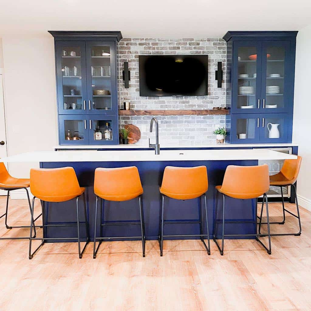 Modern wet bar with navy cabinets, brick backsplash, open shelving, and orange leather stools.