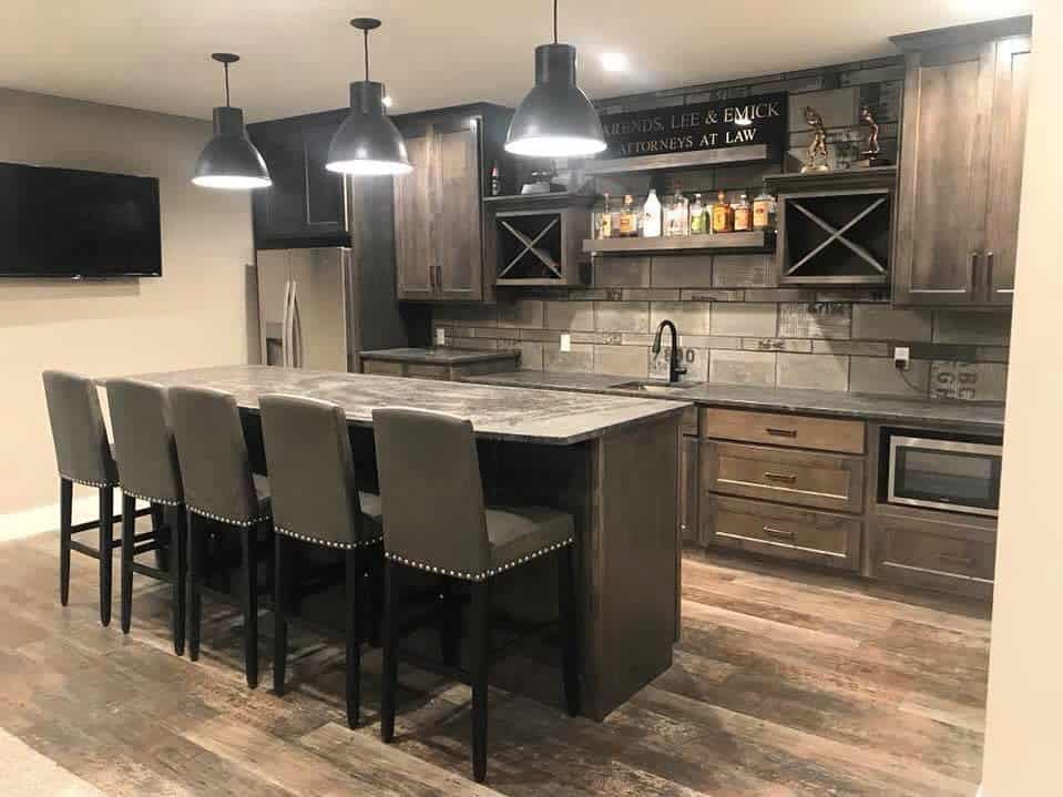 Rustic wet bar with dark wood cabinetry, tiled backsplash, pendant lighting, and upholstered stools.