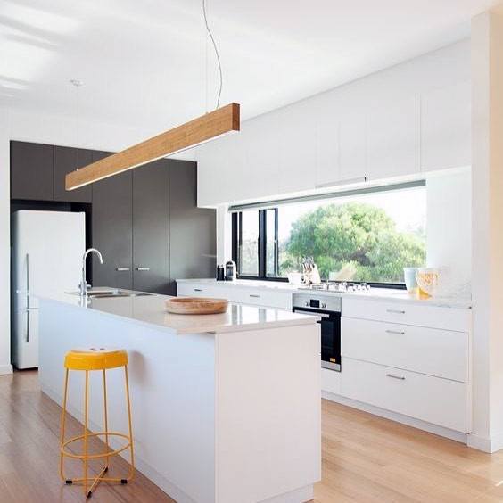 Modern kitchen featuring a long LED strip light above a white island, complemented by colorful yellow bar stools and sleek cabinetry