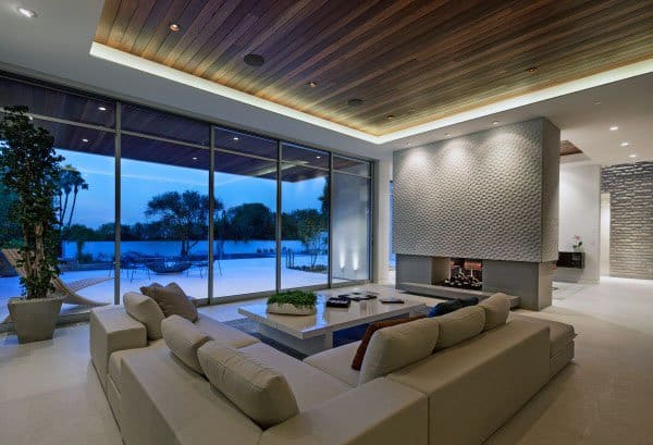 Modern living room with beige sectional sofa, large windows, and view of a pool and trees outside