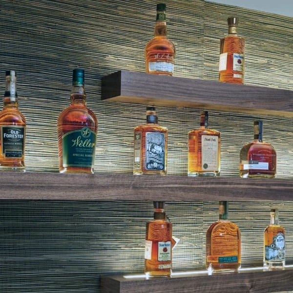 Illuminated floating shelves with whiskey bottles displayed against a textured wall.