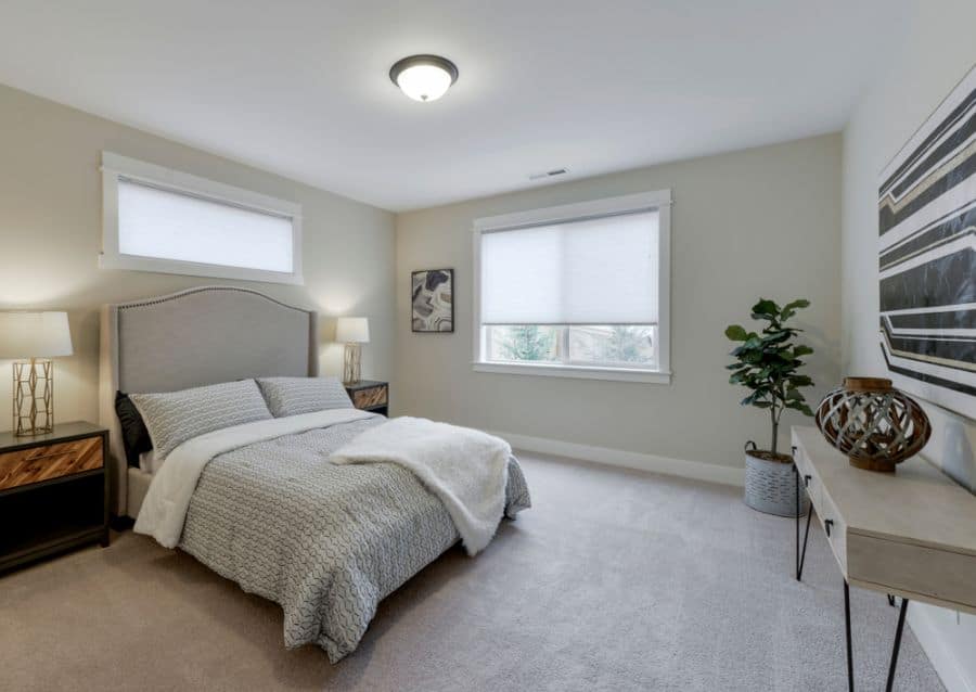 Bright bedroom with light walls, gray carpet, cozy bedding, and modern decor.