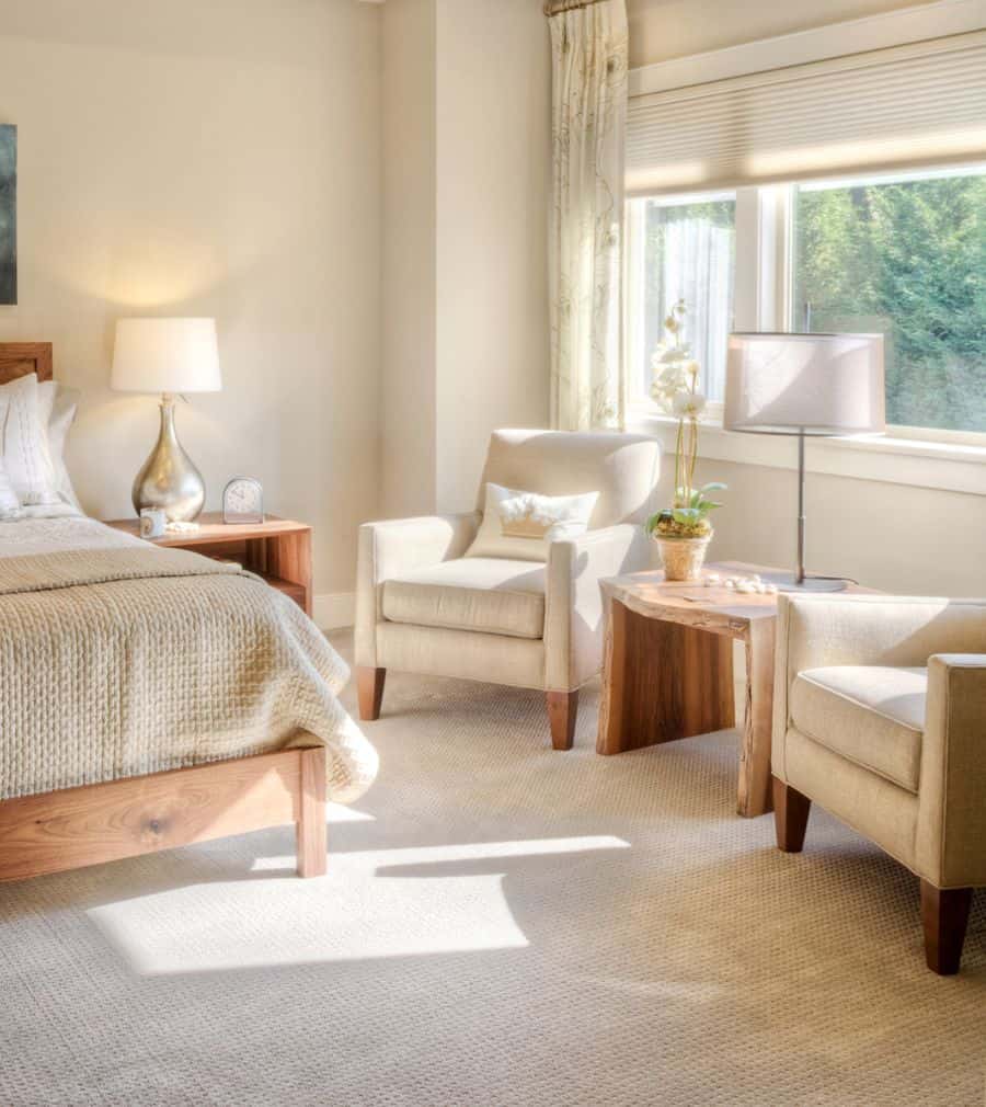 Cozy beige bedroom with lounge chairs, wooden furniture, and soft natural lighting.