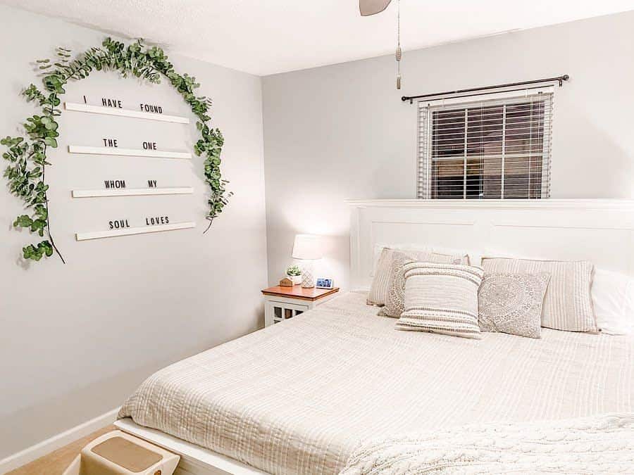 White bedroom with greenery-accented quote wall art and cozy neutral bedding.