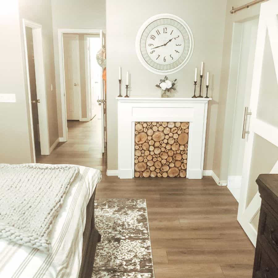 Rustic bedroom with log-filled fireplace, clock, and candles on the mantle.