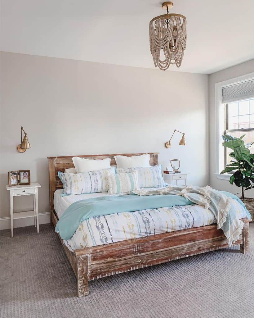 Rustic bedroom with distressed wooden bed frame, gold wall lamps, and white bedside tables.