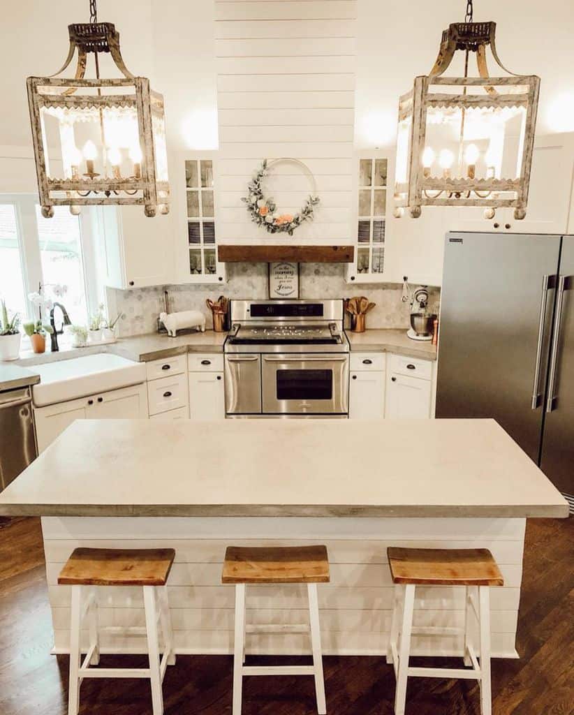 Charming farmhouse kitchen with shiplap island rustic chandeliers and white wooden stools.