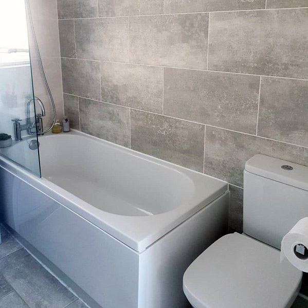 Minimalist bathroom with a bathtub, toilet, and grey tiled walls