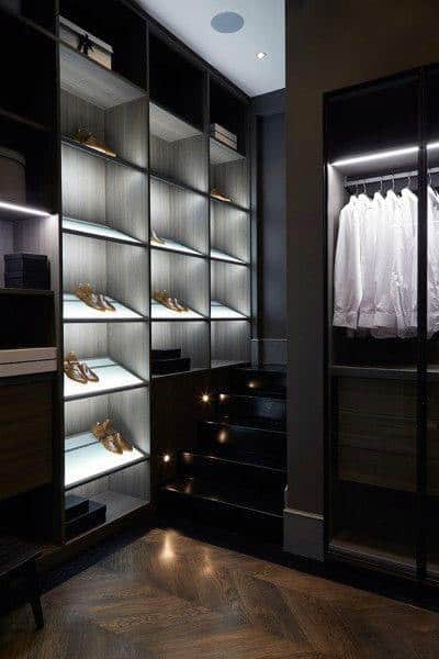 A modern closet with illuminated shoe shelves and a hanging rail with neatly arranged white shirts