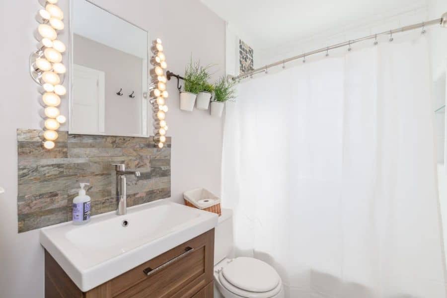 Modern bathroom with a white sink, illuminated mirror, potted plants, and a white shower curtain