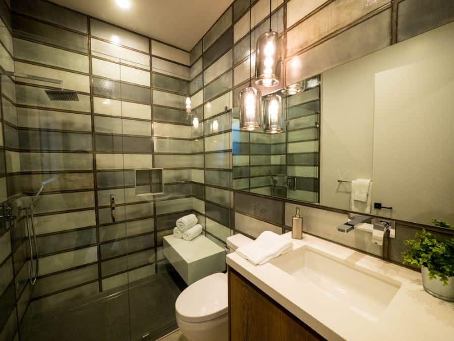 Modern bathroom with hanging pendant lights, glass shower, and horizontal tiled walls.