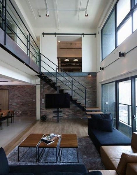 Modern living room with high ceilings, metal staircase, large windows, and minimalist decor.