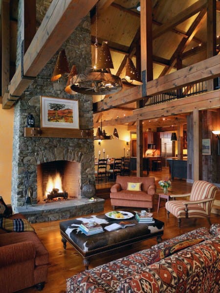 Cozy rustic living room with a stone fireplace, wooden beams, sofas, leather ottoman, and warm lighting