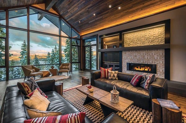 Cozy living room with large windows, dark leather sofas, a fireplace, and a view of snowy pine trees