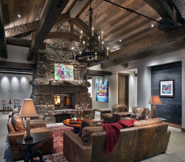 Cozy living room with exposed beams, stone fireplace, leather sofas, colorful paintings, and a chandelier