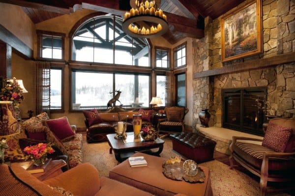 A rustic living room with a grand stone fireplace, large windows showcasing snowy views, comfortable seating, and warm decor, creating a cozy, inviting atmosphere