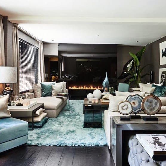 Chic living room featuring a large sectional sofa, fireplace, decorative plants, and elegant teal accents