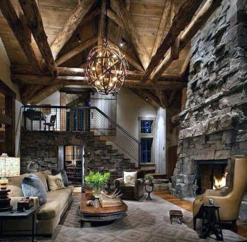 Rustic living room with exposed wooden beams, stone fireplace, leather sofas, and a decorative chandelier