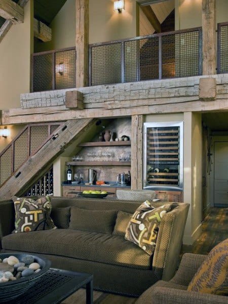 A rustic living room with a cozy sofa, exposed wooden beams, a stylish staircase, and a wine storage area, creating a warm and functional space