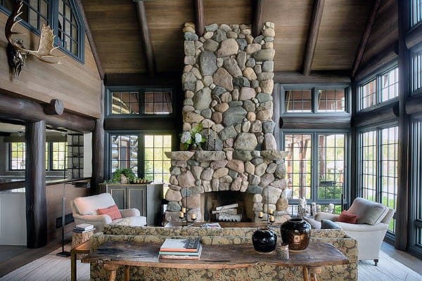 Rustic sunroom with vaulted wood ceiling, large stone fireplace, and cozy seating area.