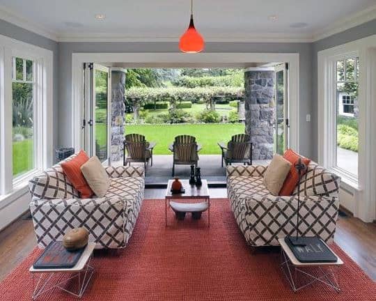 Modern sunroom with patterned sofas, red rug, open doors, and garden view.