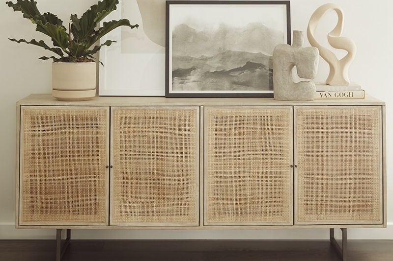 Woven rattan sideboard with abstract decor, framed artwork, and potted plant on top.