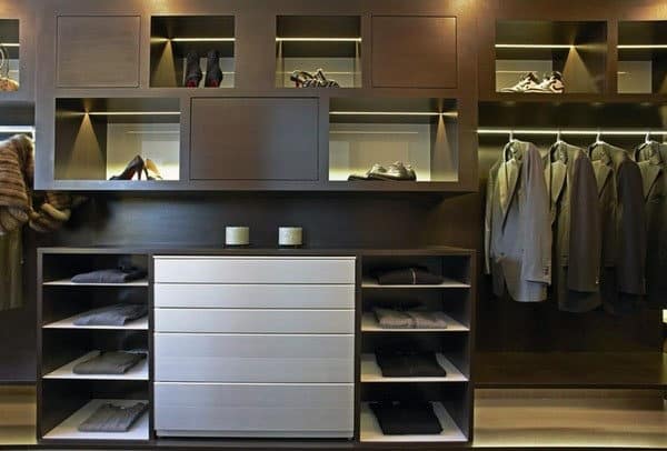 Modern walk-in closet with shelves, hanging suits, and a dresser, featuring neatly organized shoes and accessories