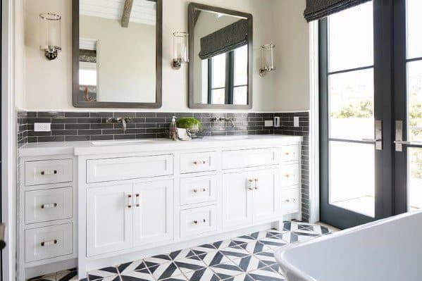 Luxury bathroom with white double vanity, black backsplash, geometric floor tiles, and mirrors.