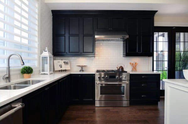 Black kitchen cabinets with white countertops, subway tile backsplash, and stainless steel appliances.