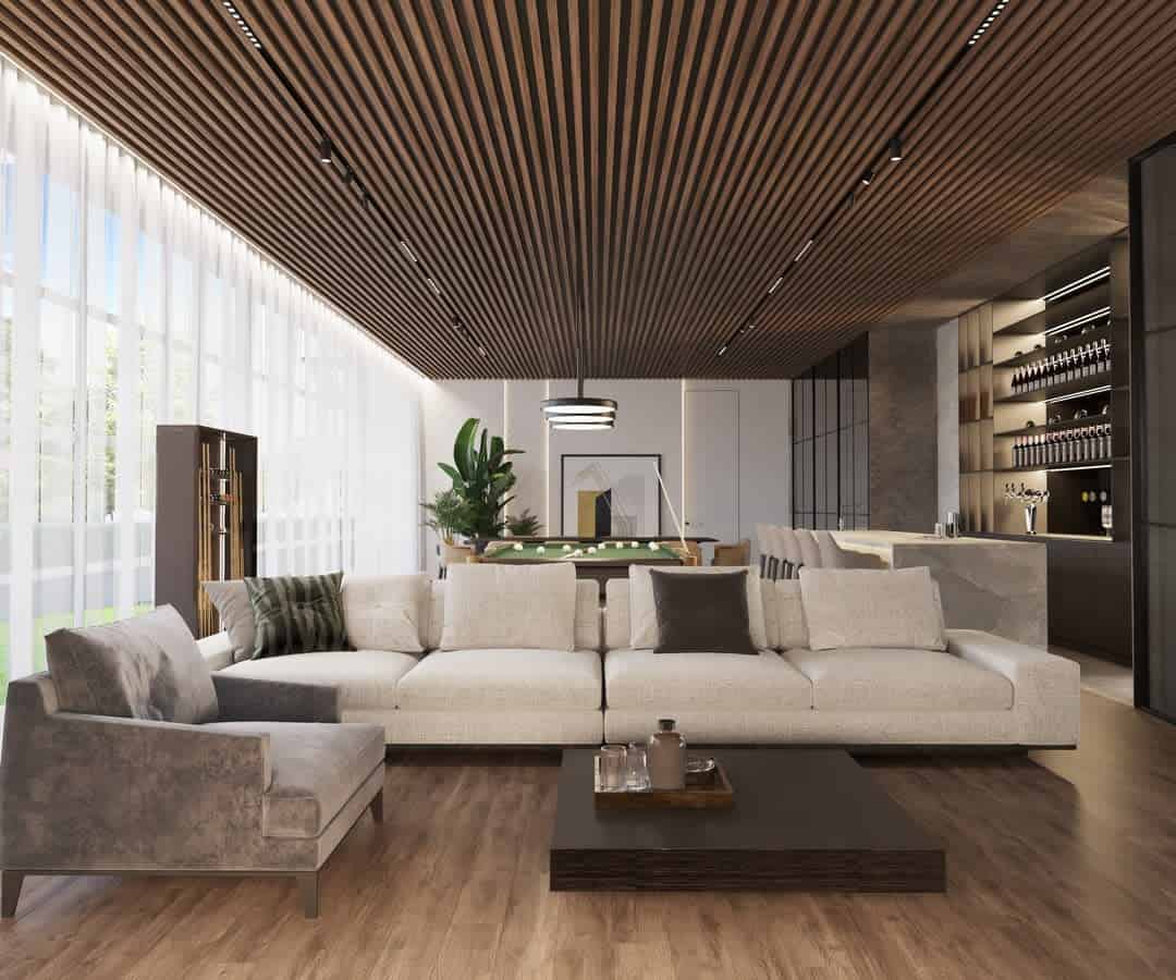 Modern living room with a large brown sofa, armchair, wooden ceiling, and floor-to-ceiling windows letting in natural light