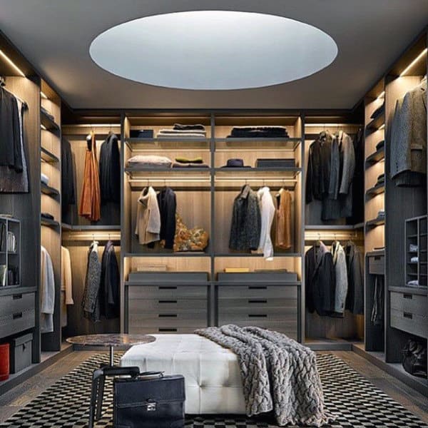 Luxurious walk-in closet with wooden shelves, clothing, a ceiling light, a central ottoman, and a patterned rug