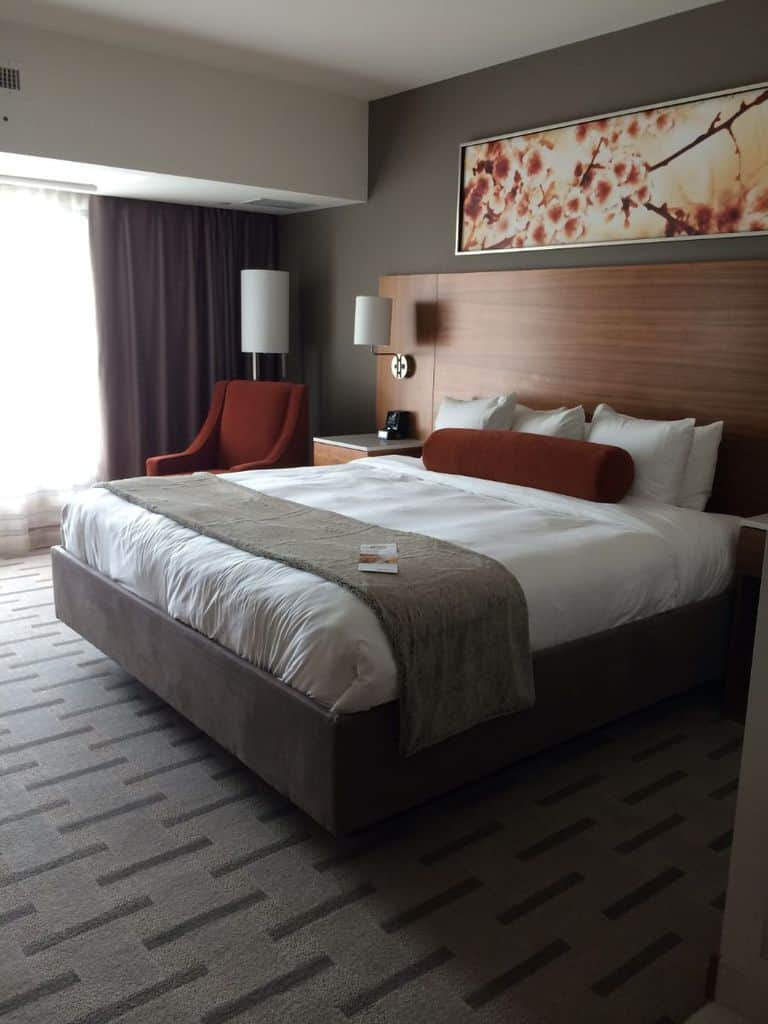 Luxury hotel room featuring a large bed with a wood headboard, dark curtains, and warm earthy tones.