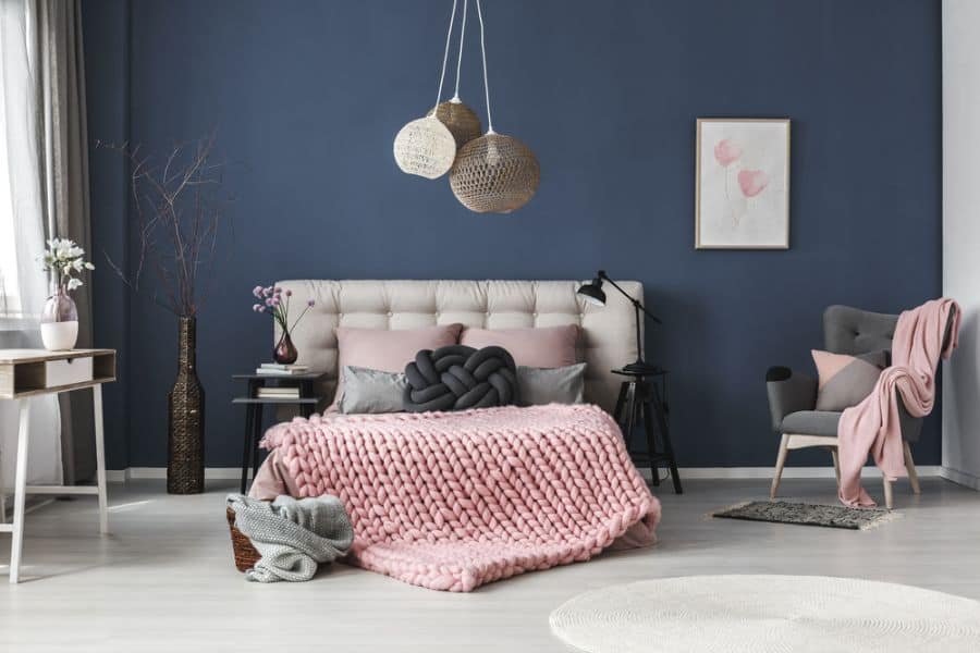 Modern bedroom with blue feature wall, pink accents, and woven hanging lights.