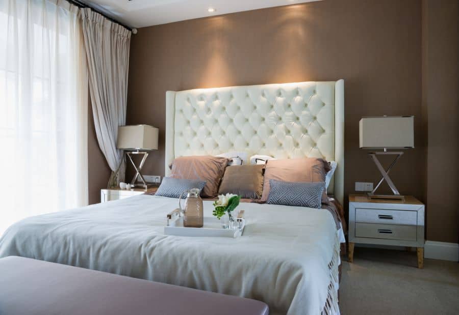 Luxury hotel-style bedroom with tufted headboard, brown feature wall, and soft lighting.