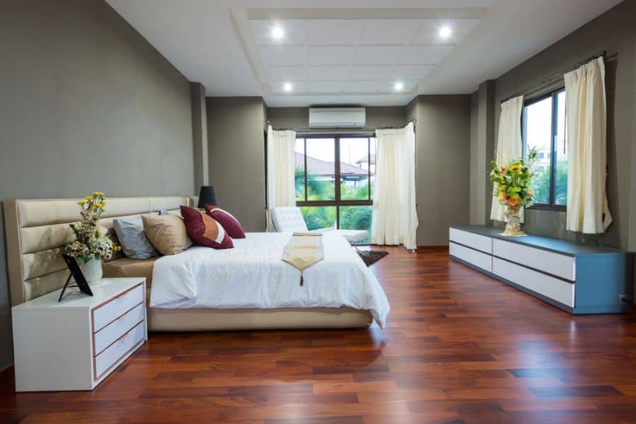 Spacious gray bedroom with modern furnishings, wooden floor, and large windows.