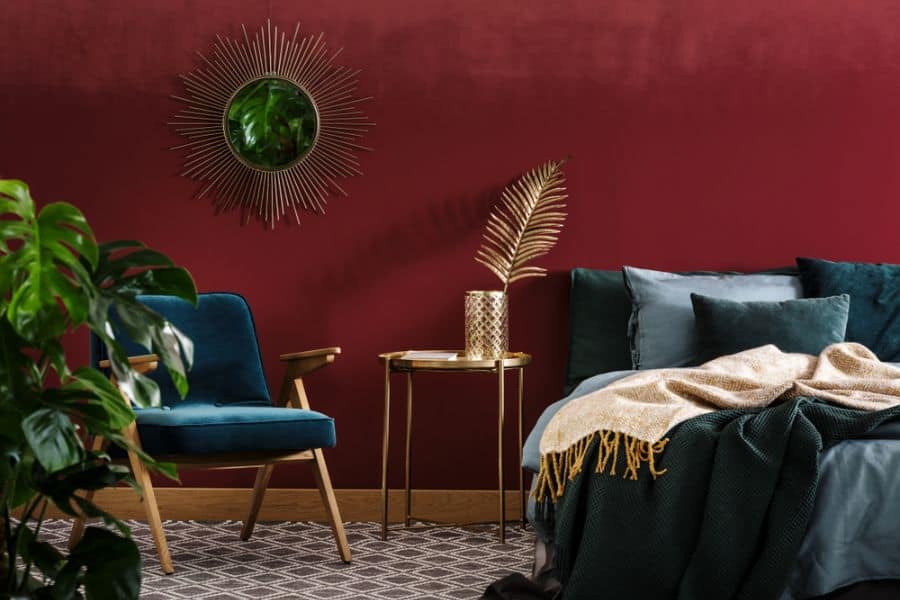 Elegant bedroom with red wall, gold accent table, blue chair, and green plants.