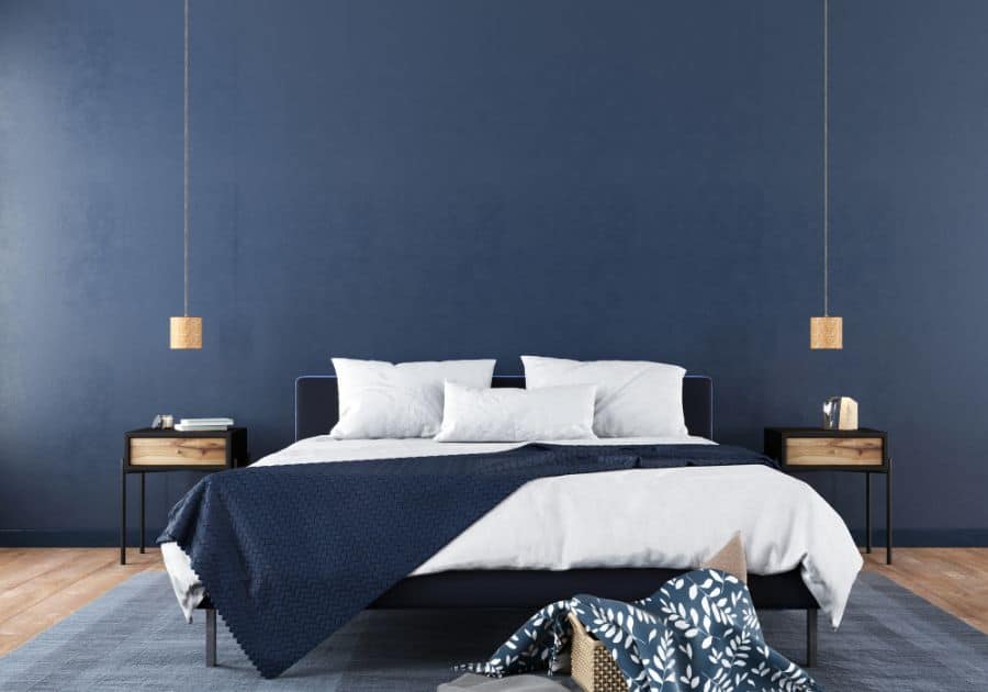 Modern blue bedroom with low-hanging pendant lights, large rug, and cozy bedding.