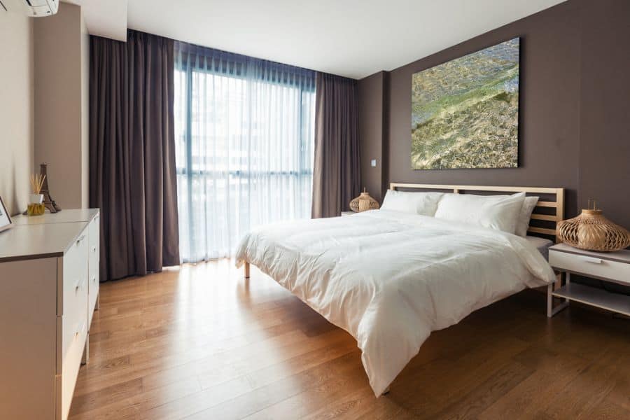 Cozy brown bedroom with hardwood floors, large wall art, and soft natural light.