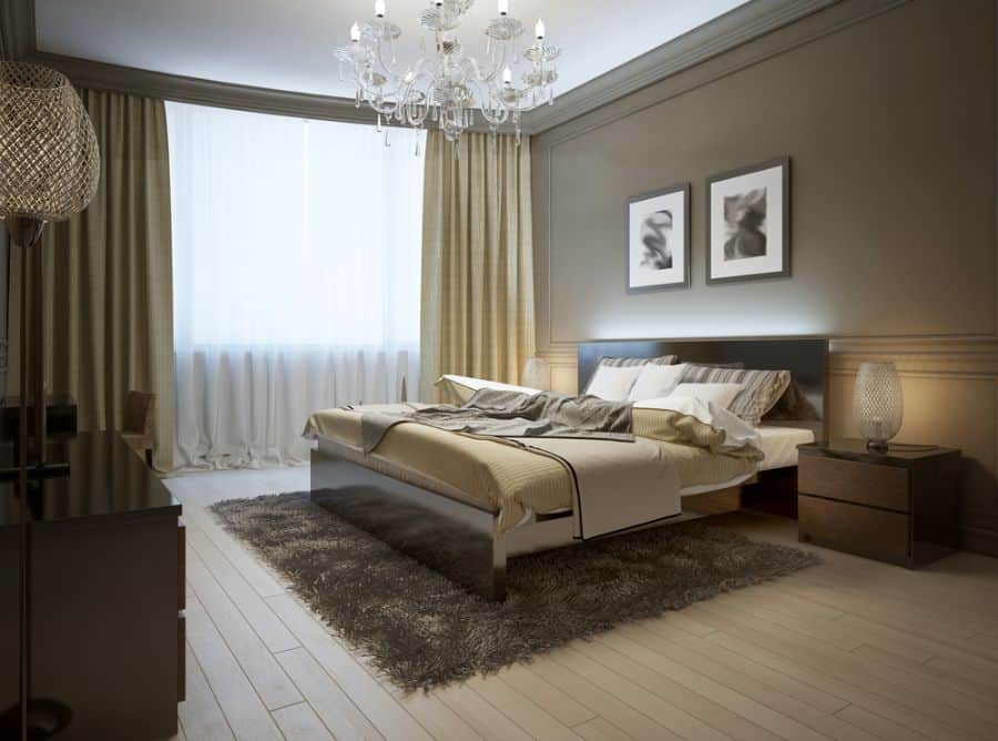 Spacious luxury bedroom with chandelier, framed wall art, rug, and elegant floorboards.