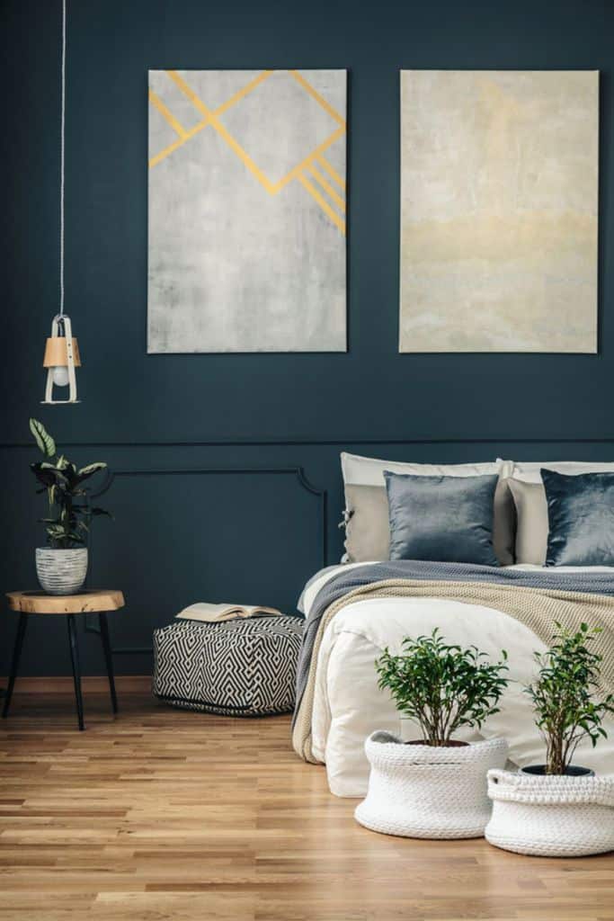 Blue bedroom with abstract wall art, timber floor, and potted plants.