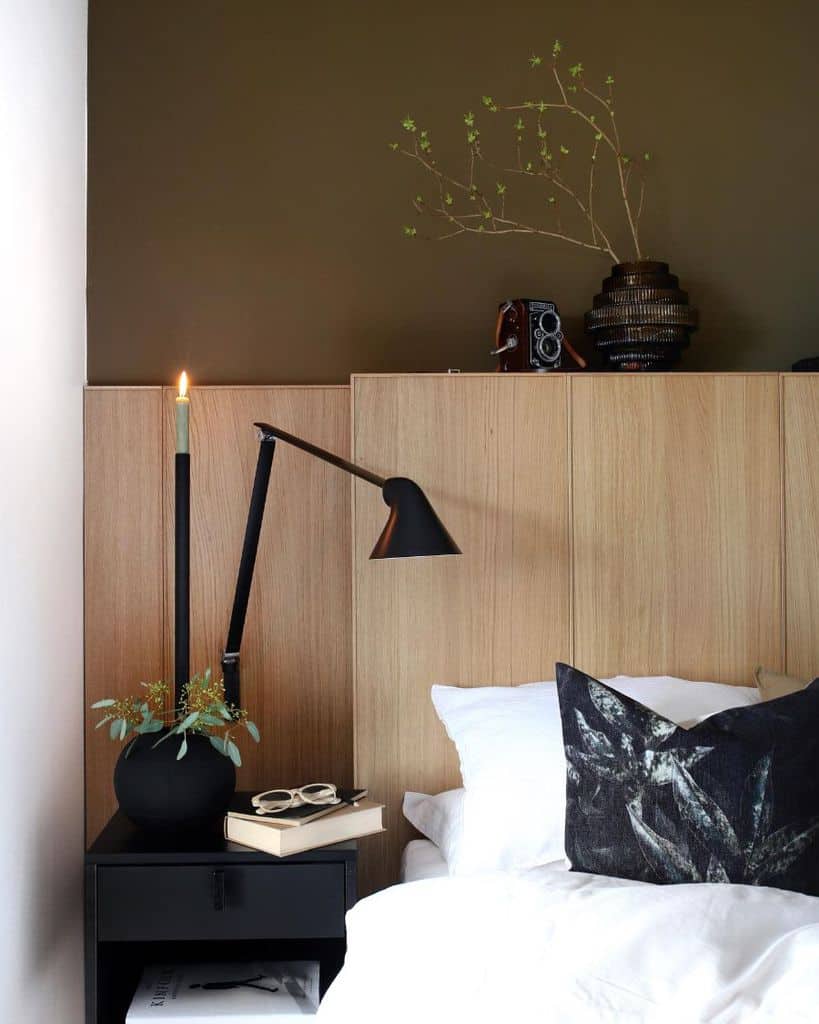 Modern bedroom with black desk lamp, candle, and decorative pillow on wooden headboard.