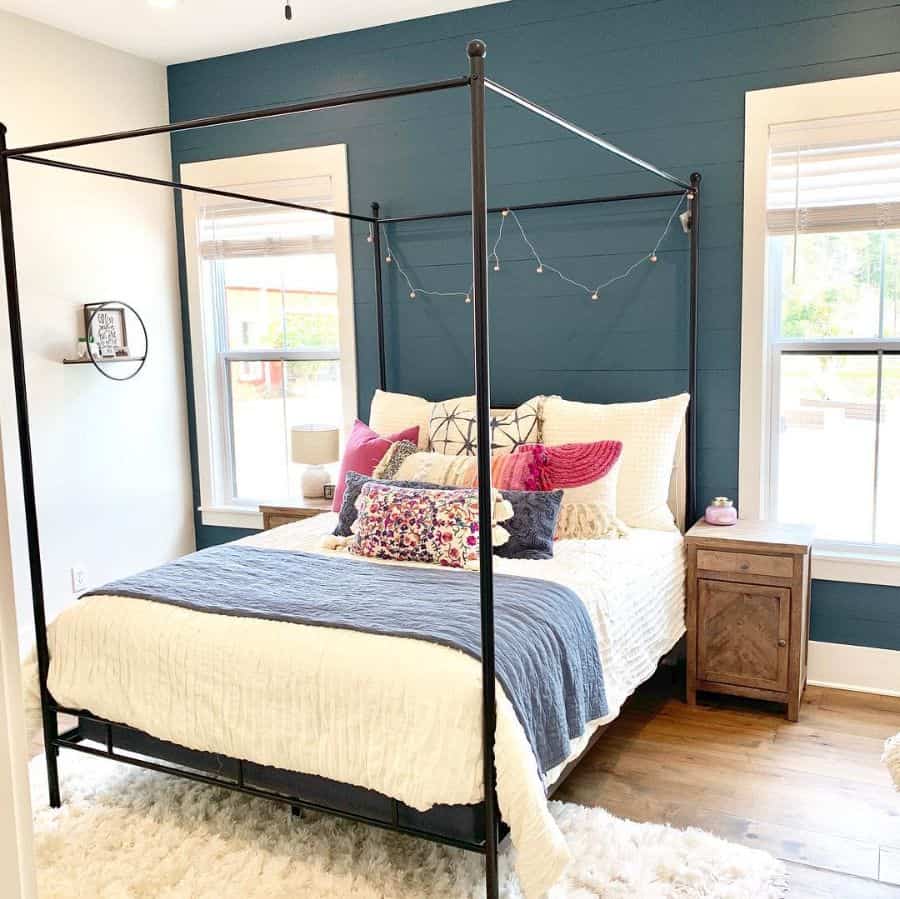 Green farmhouse bedroom with four-poster bed, colorful pillows, and white rug.