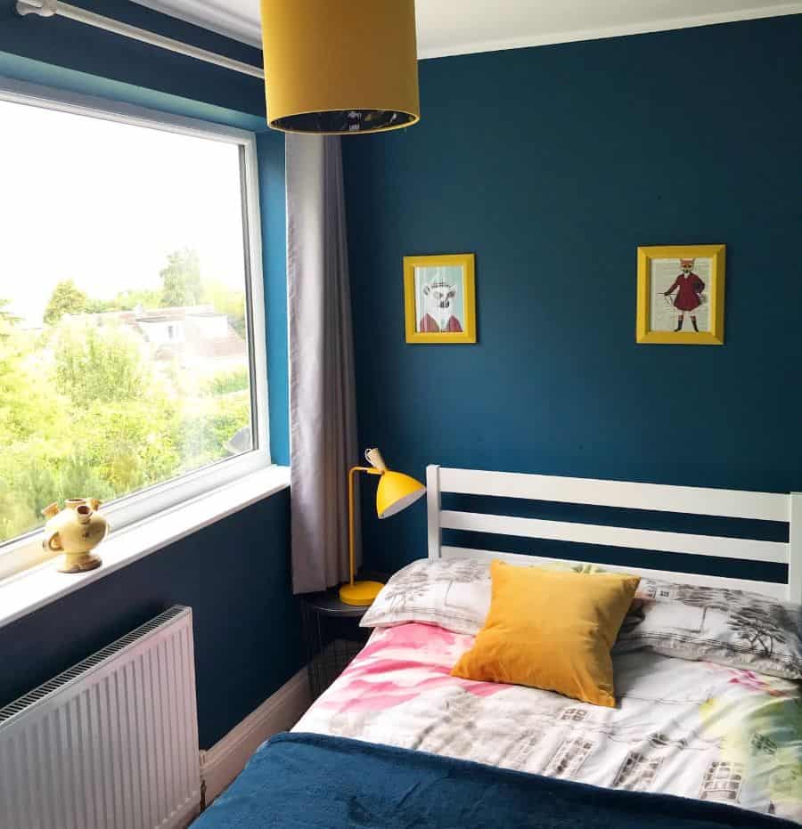 Modern green bedroom with large window, yellow lamp, and framed wall art.