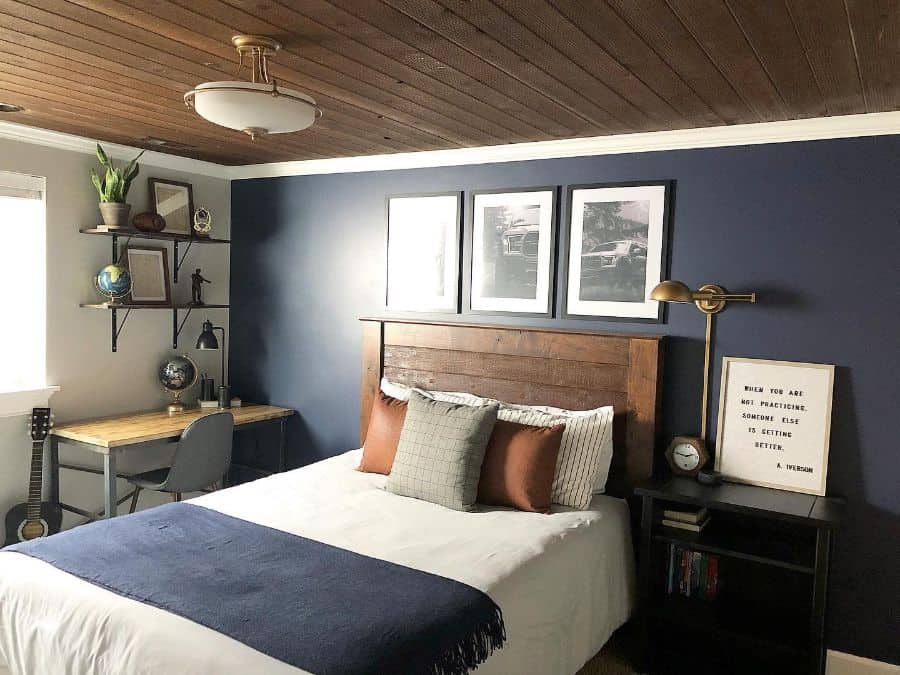 Modern men's bedroom with blue feature wall, wood panel ceiling, and workspace desk.