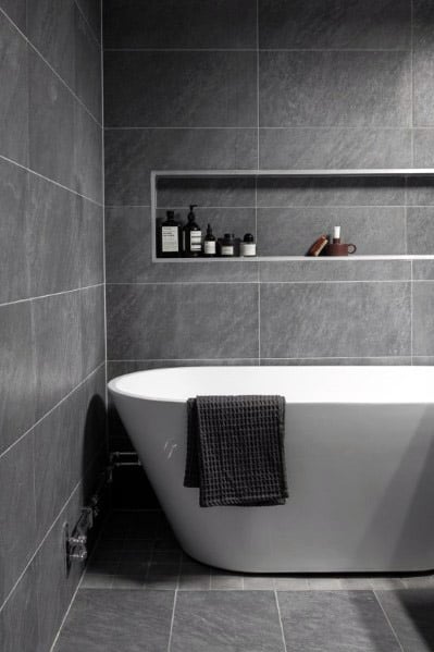 Modern bathroom with a freestanding tub, gray tiles, and a shelf with toiletries