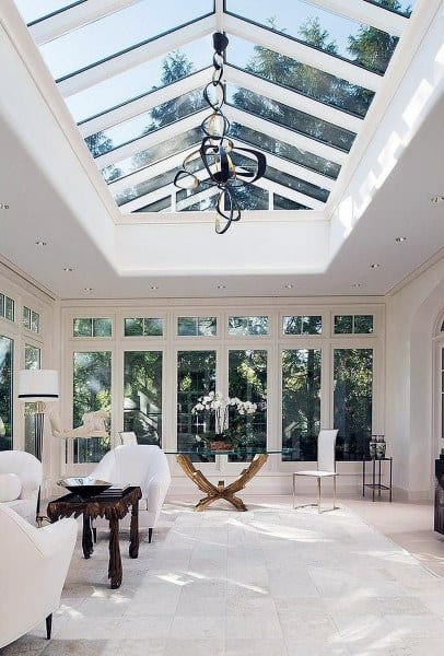 Elegant sunroom with skylight ceiling, white furniture, modern chandelier, and large windows.