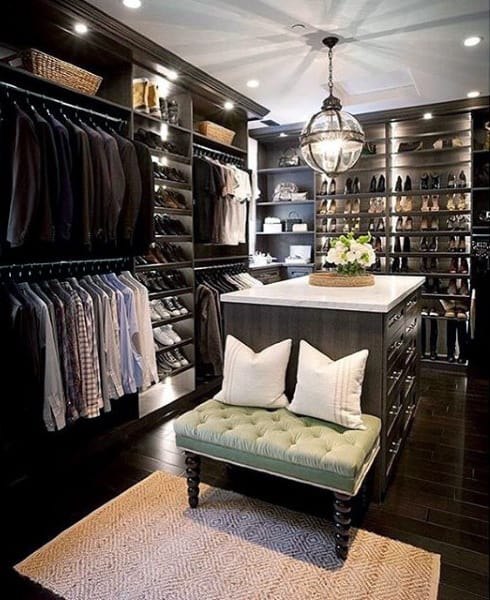 Luxurious walk-in closet with dark wood, suits, shoes, and a central island under a globe pendant light