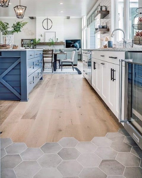 Charming kitchen featuring a combination of light hardwood flooring and hexagonal tile, with a modern blue island, white cabinetry, and elegant decor elements