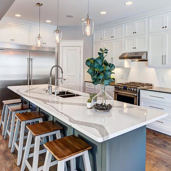 Elegant kitchen with pendant lighting above a marble island, complemented by wooden bar stools, modern appliances, and sleek white cabinetry