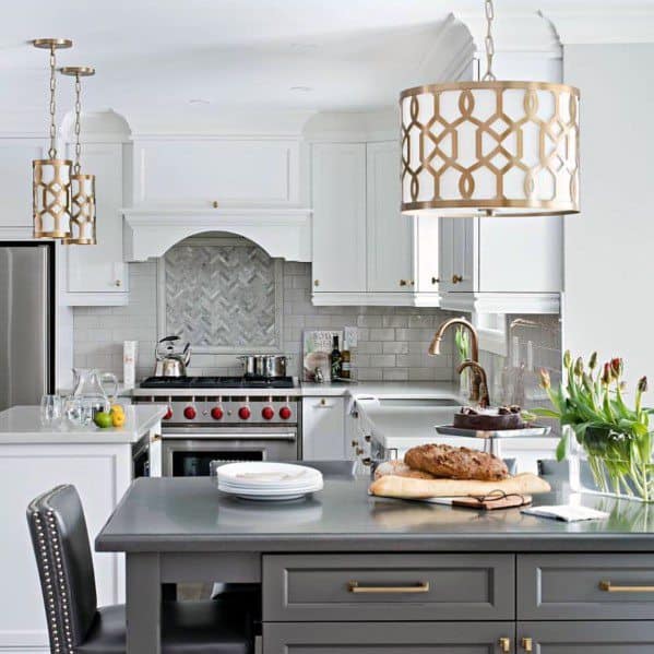 Elegant kitchen with luxurious gold pendant lighting above a dark island, complemented by white cabinetry, marble backsplash, and modern appliances